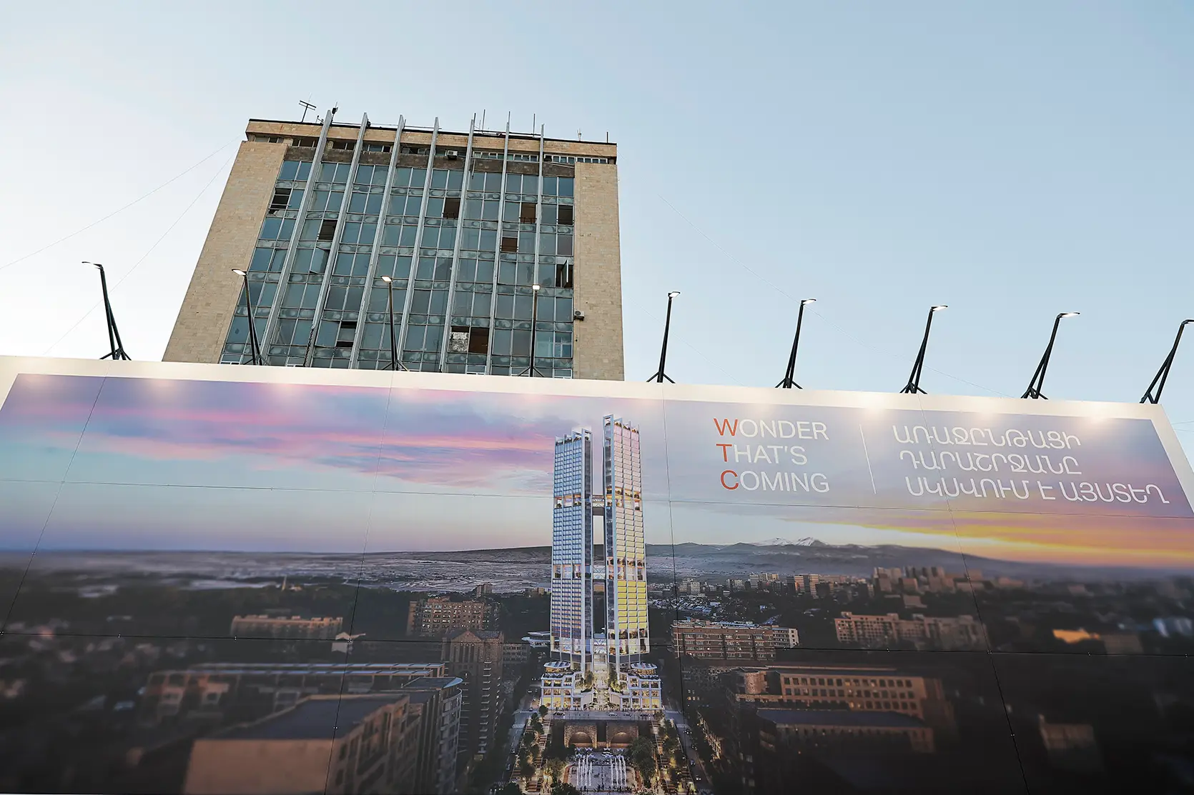 L’ancienne tour de Haypost au 22 rue Saryan, dont de nombreuses vitres manquent, derrière une palissade de chantier où est imprimée une visualisation des deux tours prévues du WTC Yerevan, 10 octobre 2026