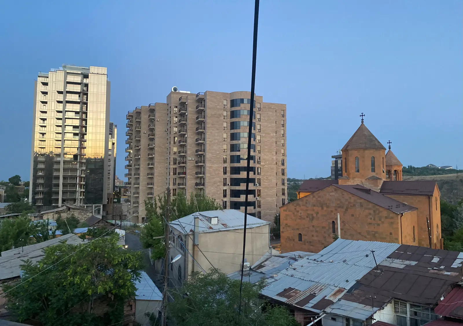 Vue au crépuscule par-dessus les vieux toits de tôle de Kond, avec à droite l’église en tuf orangé Surb Hovhannes et sa coupole conique, à gauche deux tours d’habitation modernes