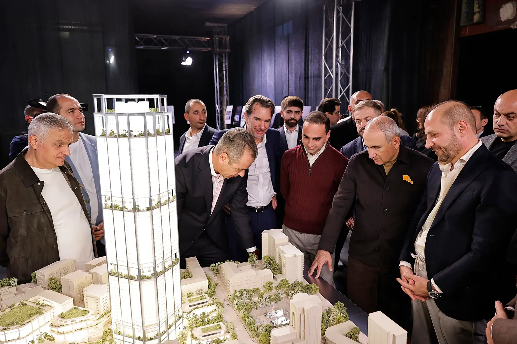 Le Premier ministre Nikol Pashinyan et d’autres invités autour d’une maquette d’architecture : une maquette blanche des tours, éclairée de l’intérieur, avec des terrasses plantées à plusieurs niveaux, au-dessus d’une maquette blanche des îlots environnants, avec des arbres et une place centrale