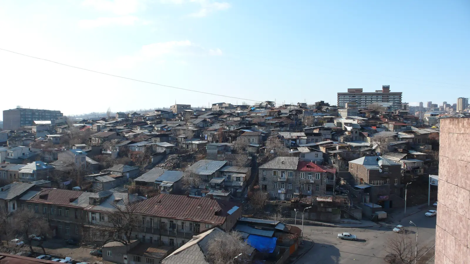 Vue hivernale en hauteur d’une colline couverte de maisons basses aux toits de tôle grise, avec au premier plan d’anciens immeubles de deux étages en tuf et à l’horizon des barres de la fin de l’époque soviétique